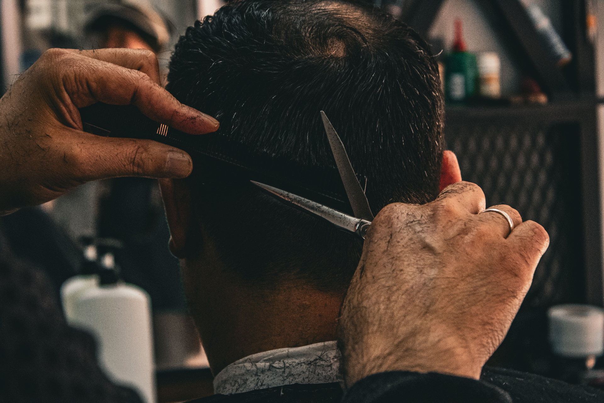 Close-up of a barber cutting a client's hair with scissors and comb — the craft that pays the rent every week.