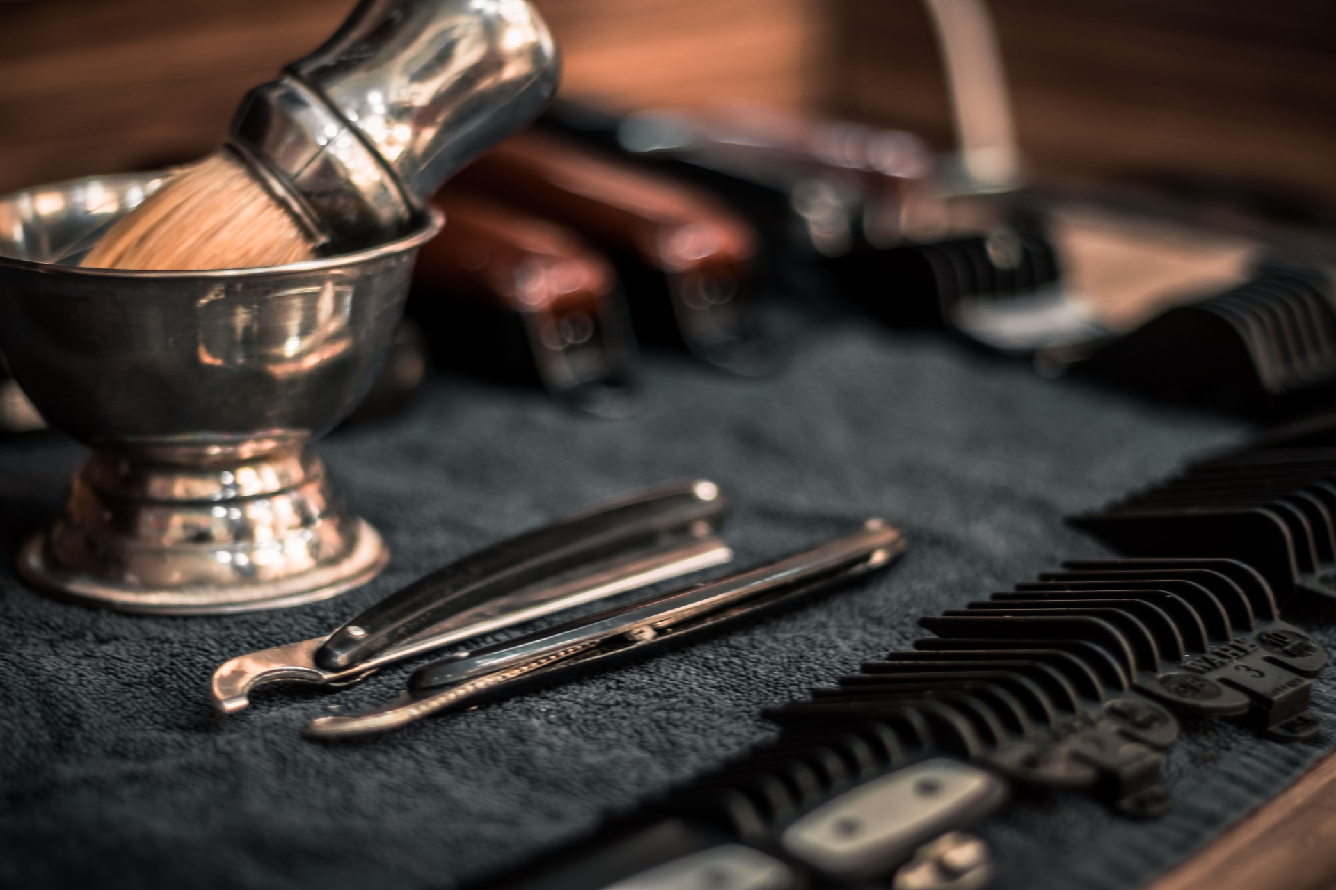 A barber's straight razor, shave brush, and clipper guards laid out on a leather roll — the tools of an independent barber.