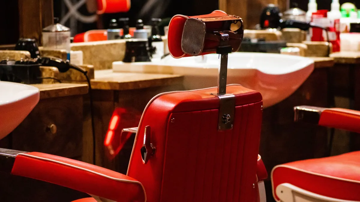 A red vintage barber chair with chrome headrest in front of a wash basin — the kind of chair you buy when a suite comes empty.