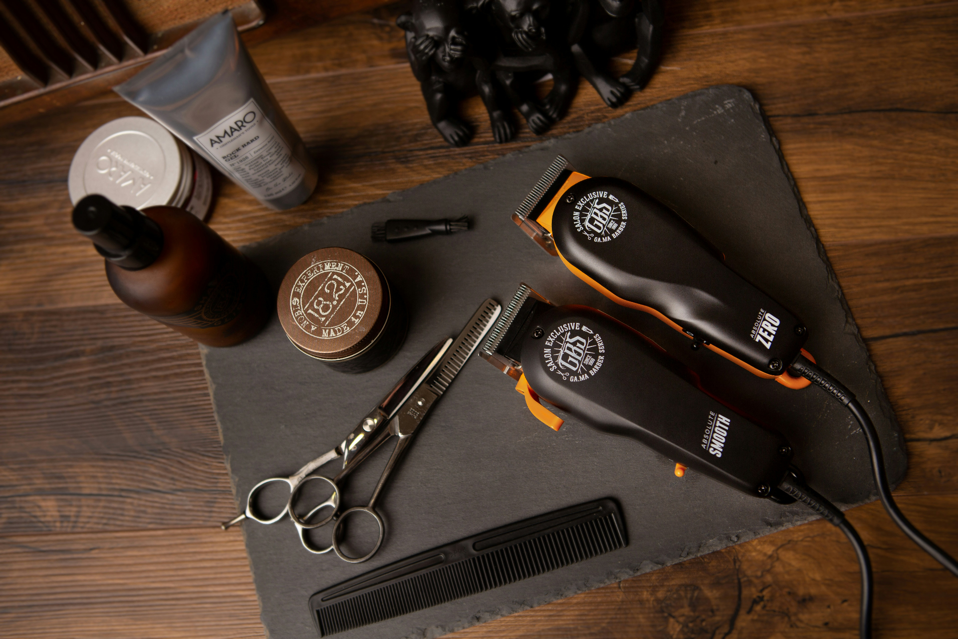 A barber's tools laid out on a slate board — clippers, shears, comb, and pomade.