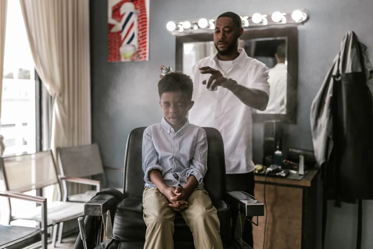 A barber finishing a young client's haircut with a spray bottle in a modern shop.