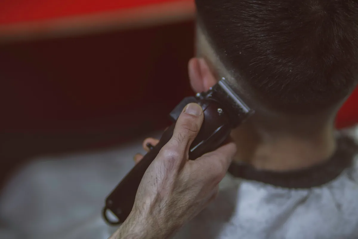 A barber using clippers to line up a client's neck and fade.
