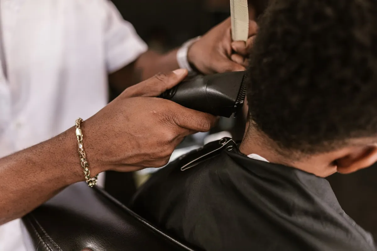 A barber lining up a client's neck with clippers and a comb.