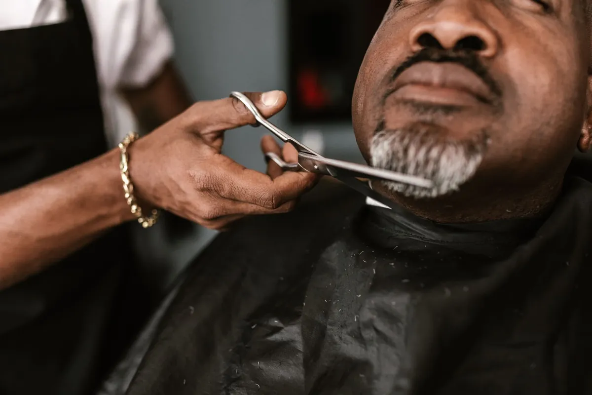 A barber trimming a client's beard with shears in a private room.