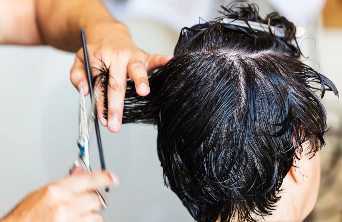 Close-up of a barber sectioning wet hair with a comb and shears.
