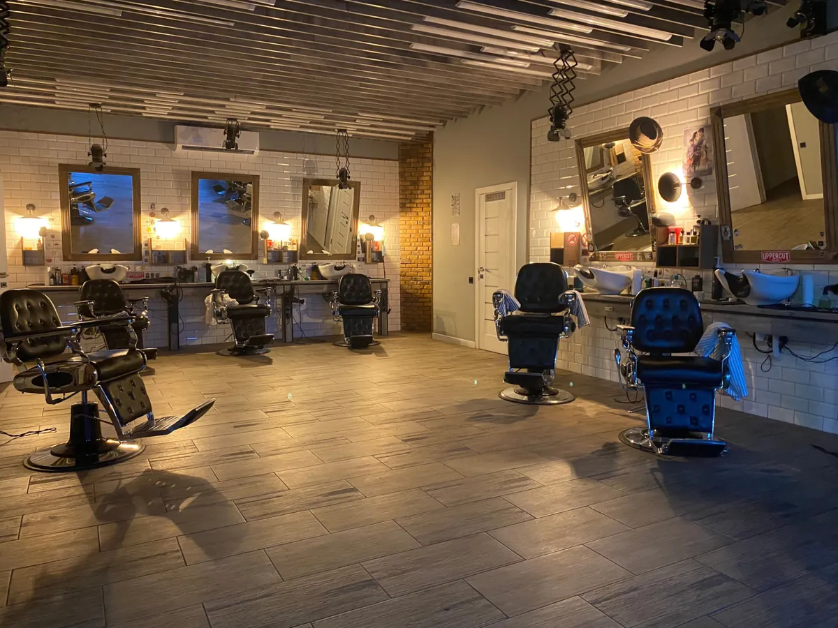 A warmly lit modern barbershop with spaced-out chairs, brick accents, and framed mirrors — the feel of a private suite setup.