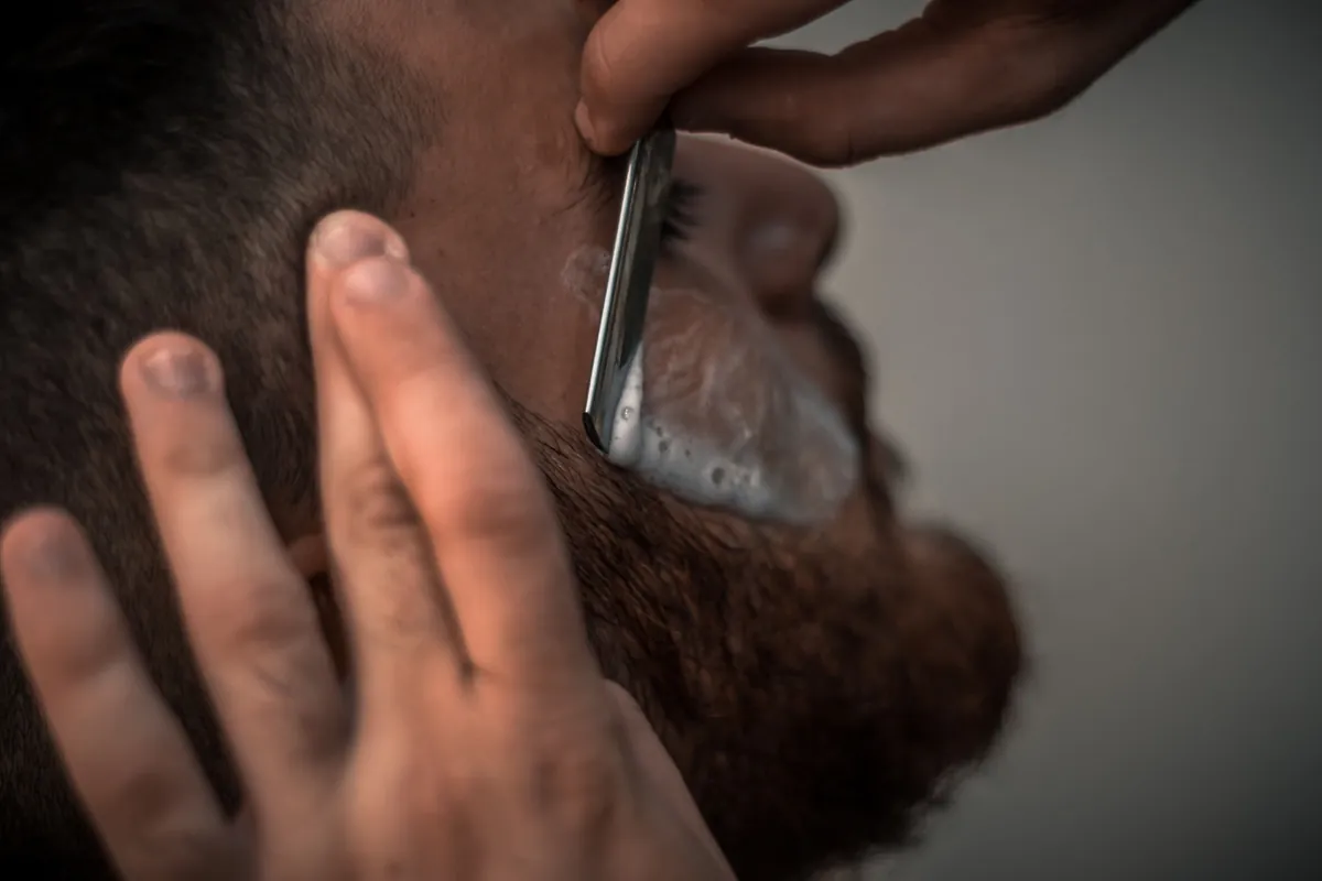 A barber giving a straight-razor shave to a bearded client.